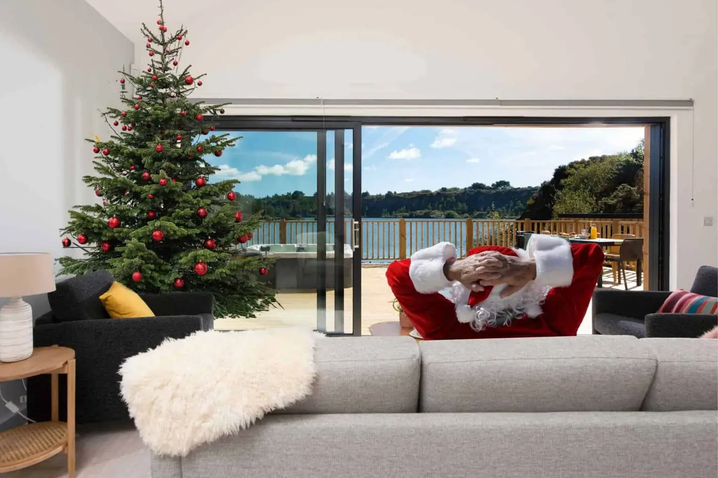 Santa relaxes on a sofa in Bradbury House, looking past a Christmas tree to the view of Trevassack Lake, Cornwall